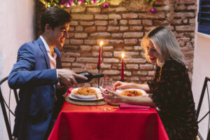 Smiling mid adult man surprising his girlfriend with a gift she is opening on a romantic date.